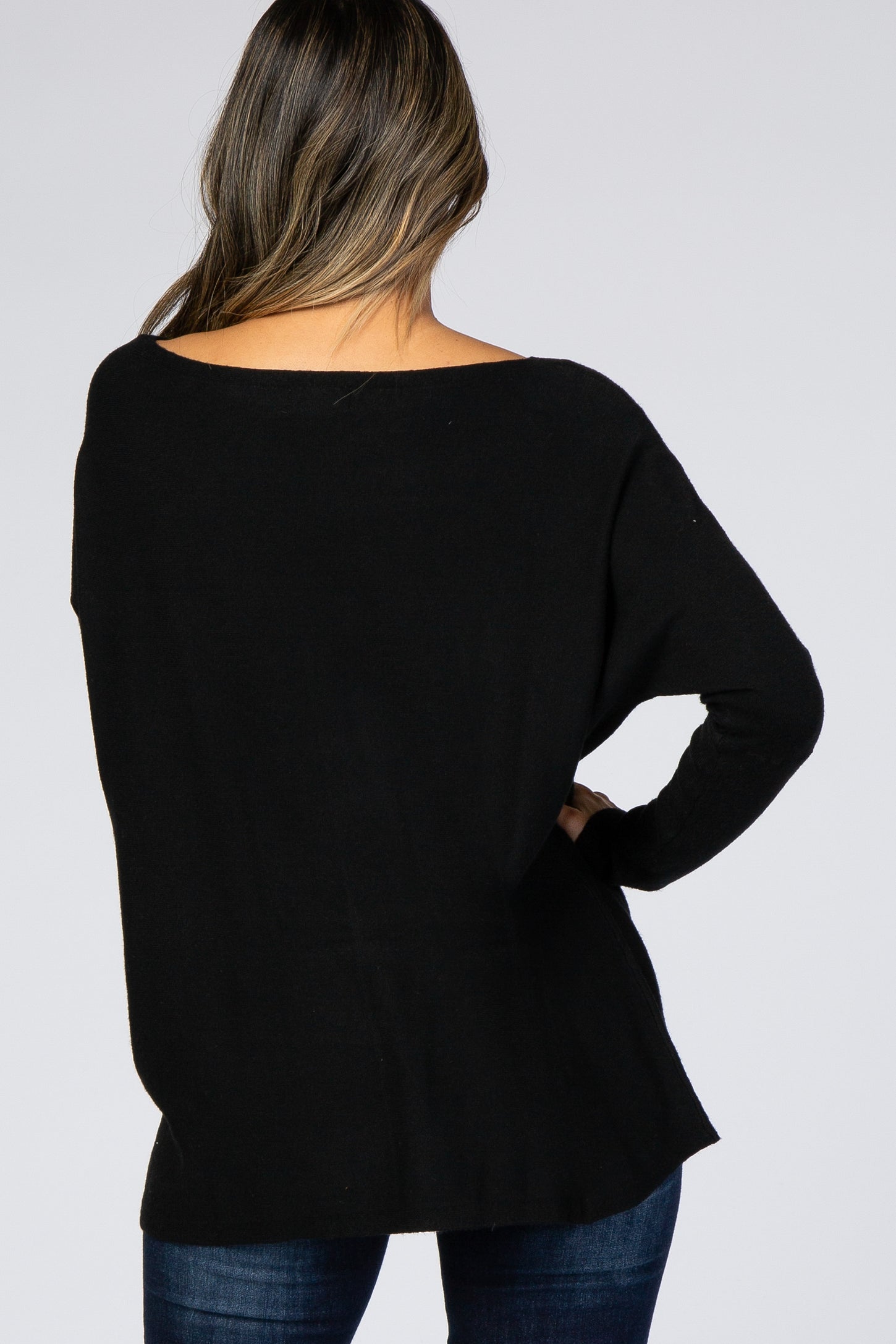 woman wearing a black oversized sweater with a wide neckline, styled with dark blue jeans