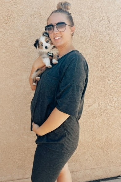 smiling pregnant woman in charcoal grey maternity dress holding a small australian shepherd puppy