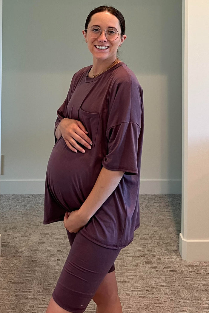 woman wearing a mauve oversized maternity t-shirt and matching bike shorts, gently cradling her baby bump