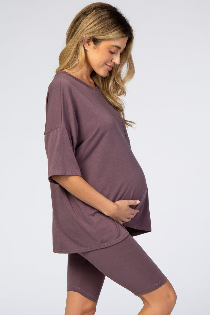 woman wearing a mauve oversized maternity tee and matching bike shorts, cradling her baby bump