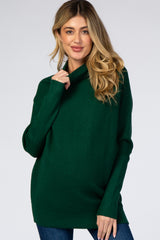 woman wearing a dark green oversized maternity sweater with a cowl neck and long sleeves