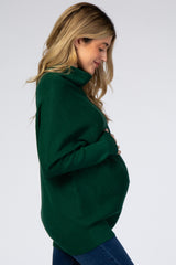 woman wearing a dark green oversized maternity sweater and holding her baby bump