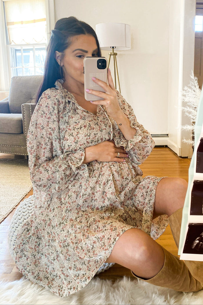 pregnant woman in floral maternity dress taking mirror selfie while holding baby bump
