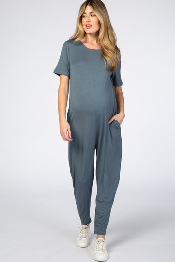 woman wearing a teal short sleeve maternity jumpsuit with side pockets and a visible baby bump