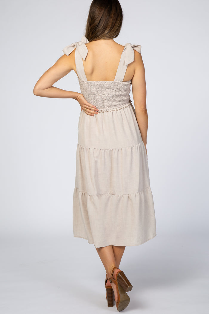 woman wearing a beige maternity dress with smocked bodice and tie straps, showing the back view