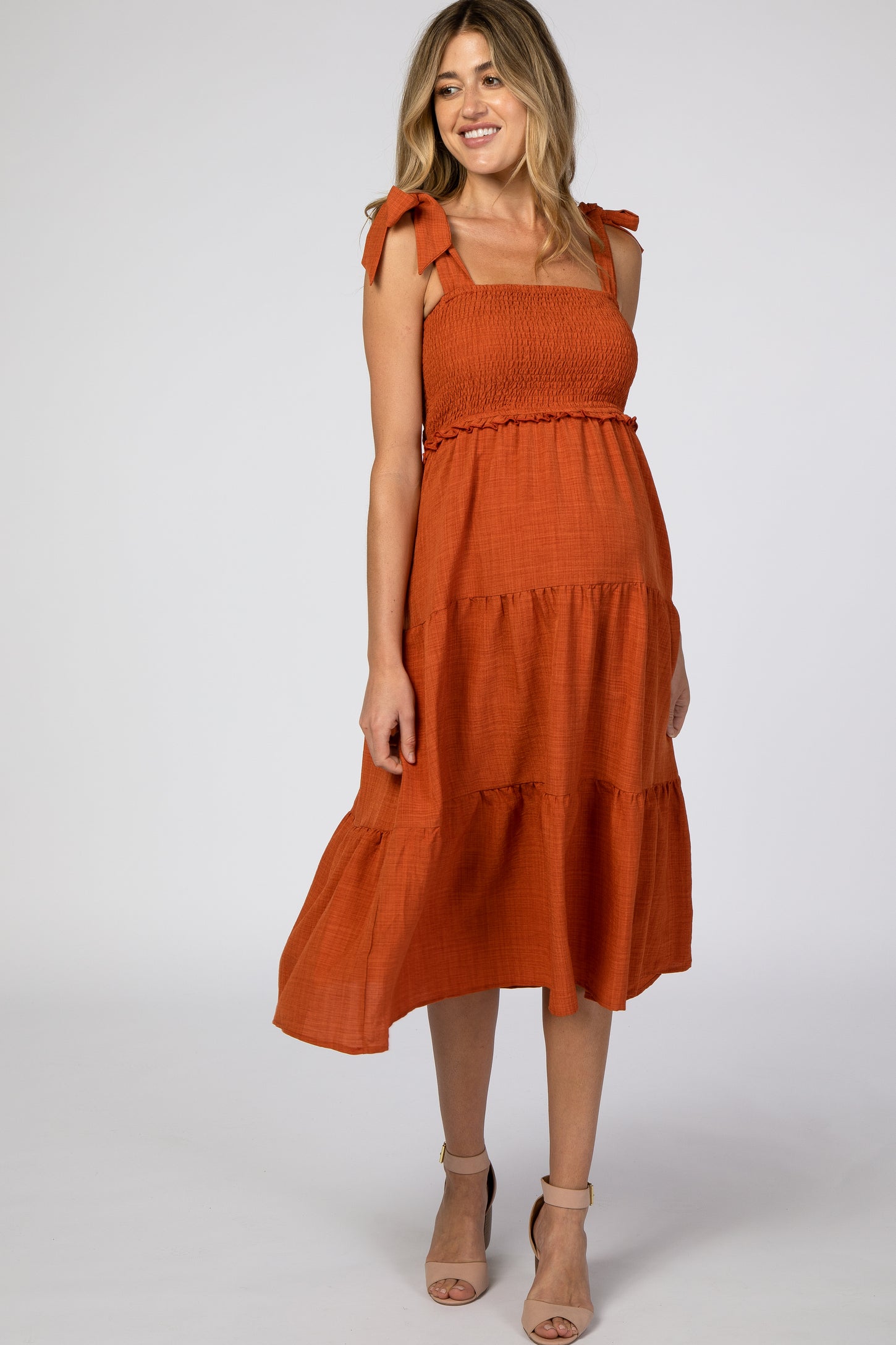 woman wearing an orange maternity dress with tie straps and tiered ruffle hemline, showcasing a baby bump
