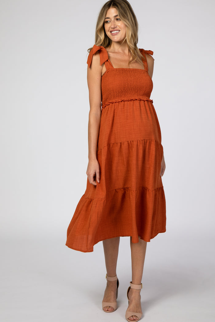 woman wearing an orange maternity dress with tie straps and tiered ruffle hemline, showcasing a baby bump