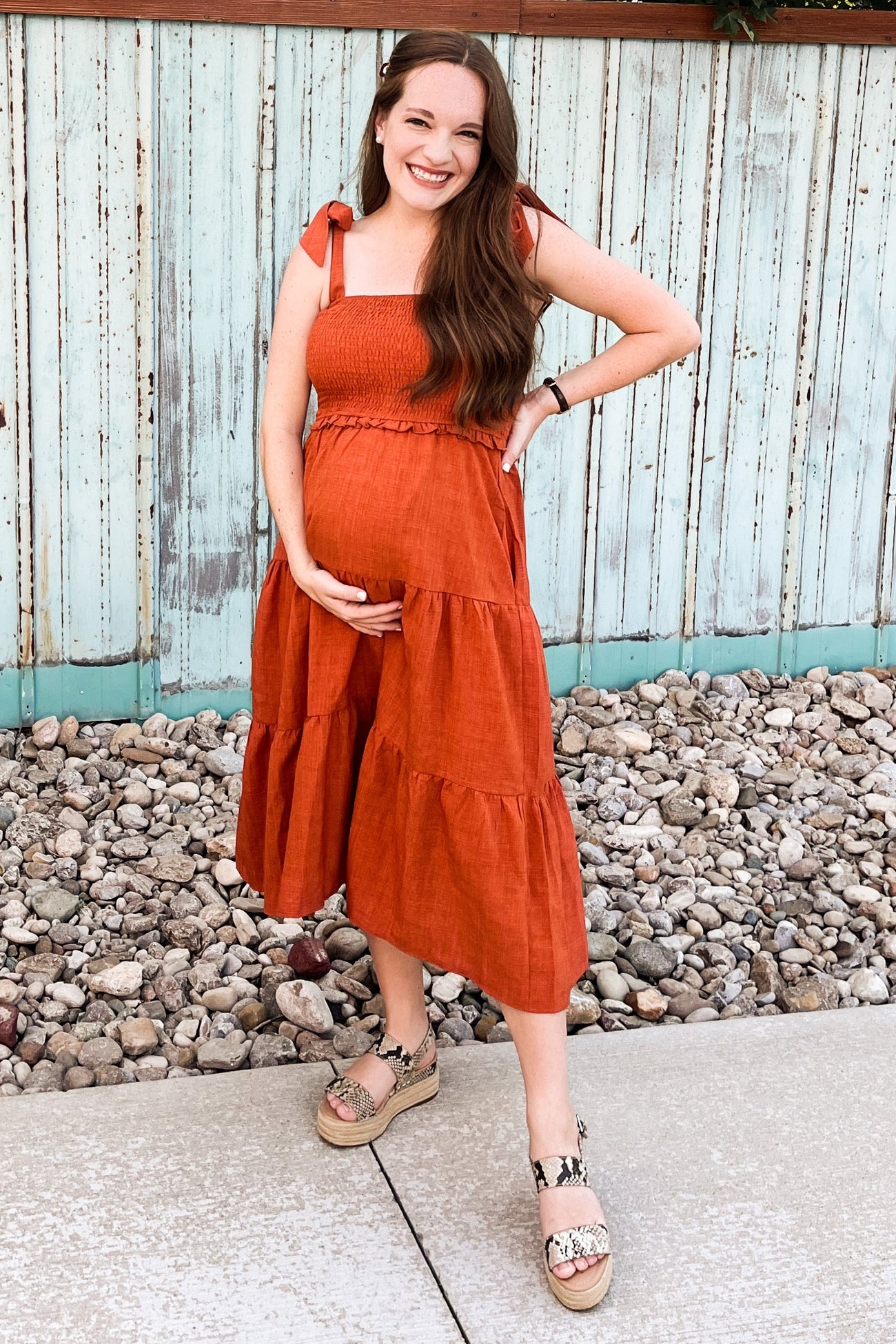 woman wearing a rusty orange maternity sundress with tiered layers and holding her baby bump