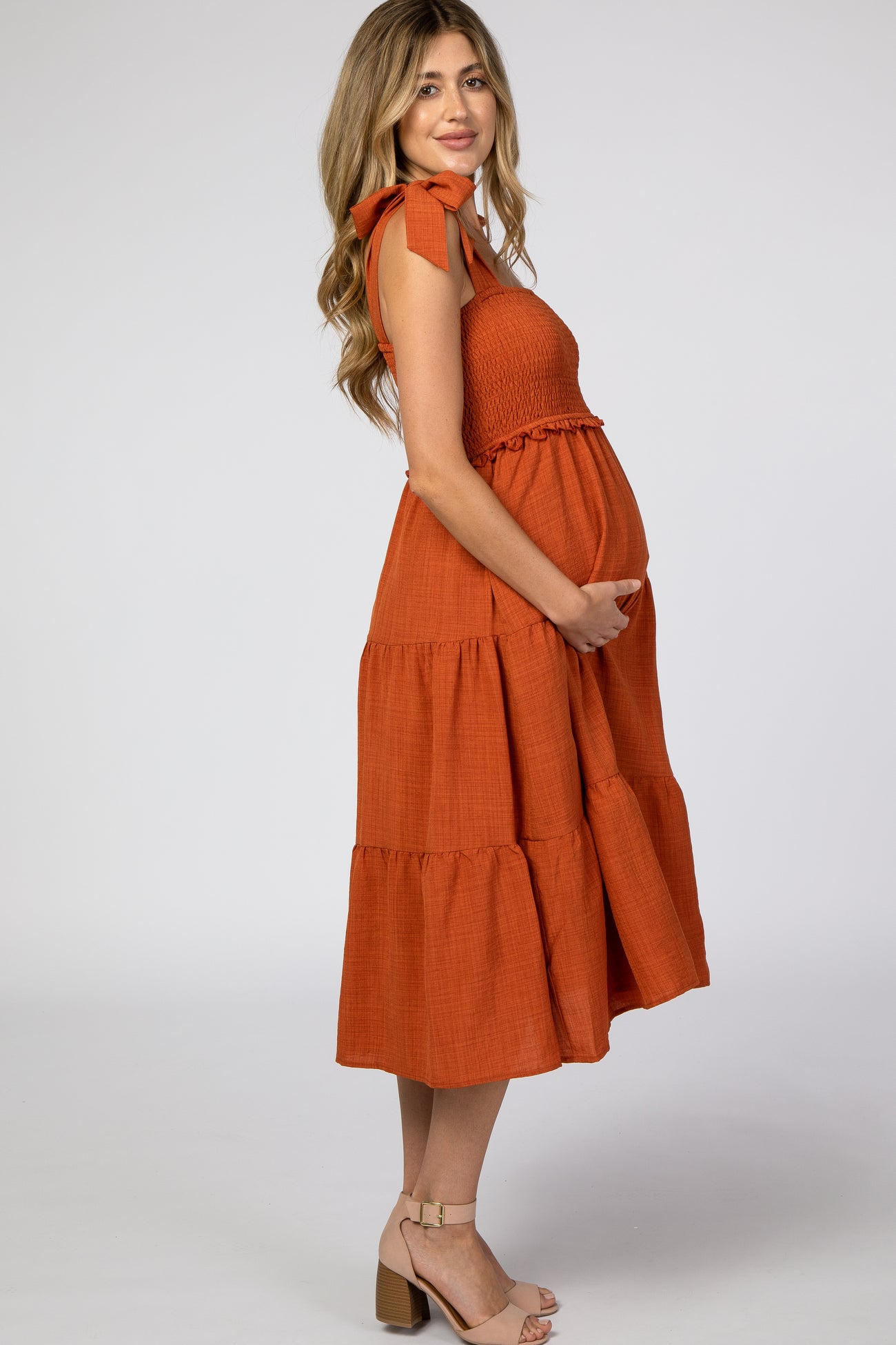 woman wearing an orange maternity dress with bow details and a tiered skirt, holding her baby bump
