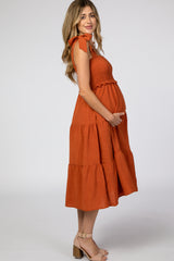 woman wearing an orange maternity dress with bow details and a tiered skirt, holding her baby bump
