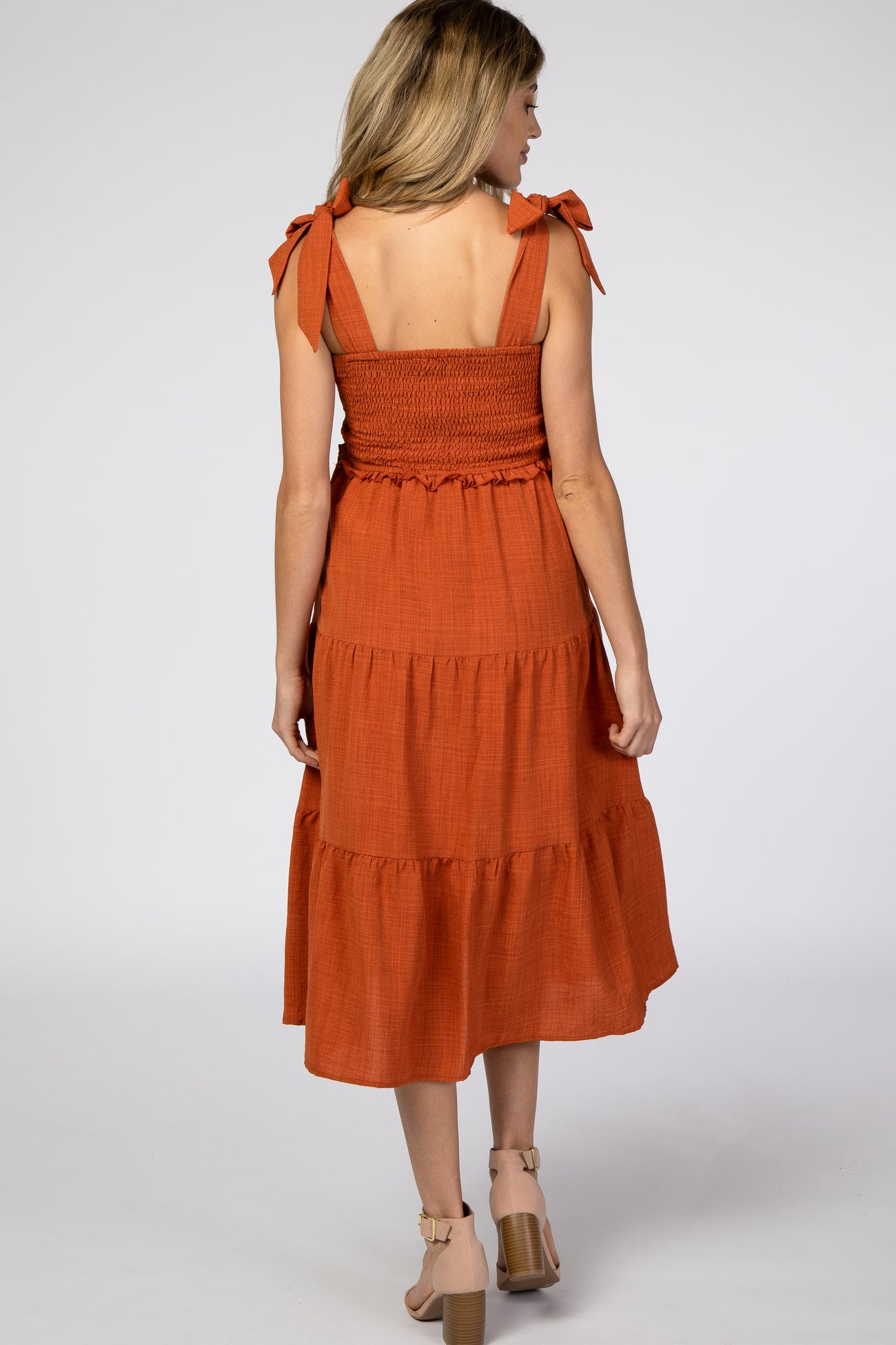 woman wearing an orange maternity dress with tie straps and a tiered skirt, showing the back view