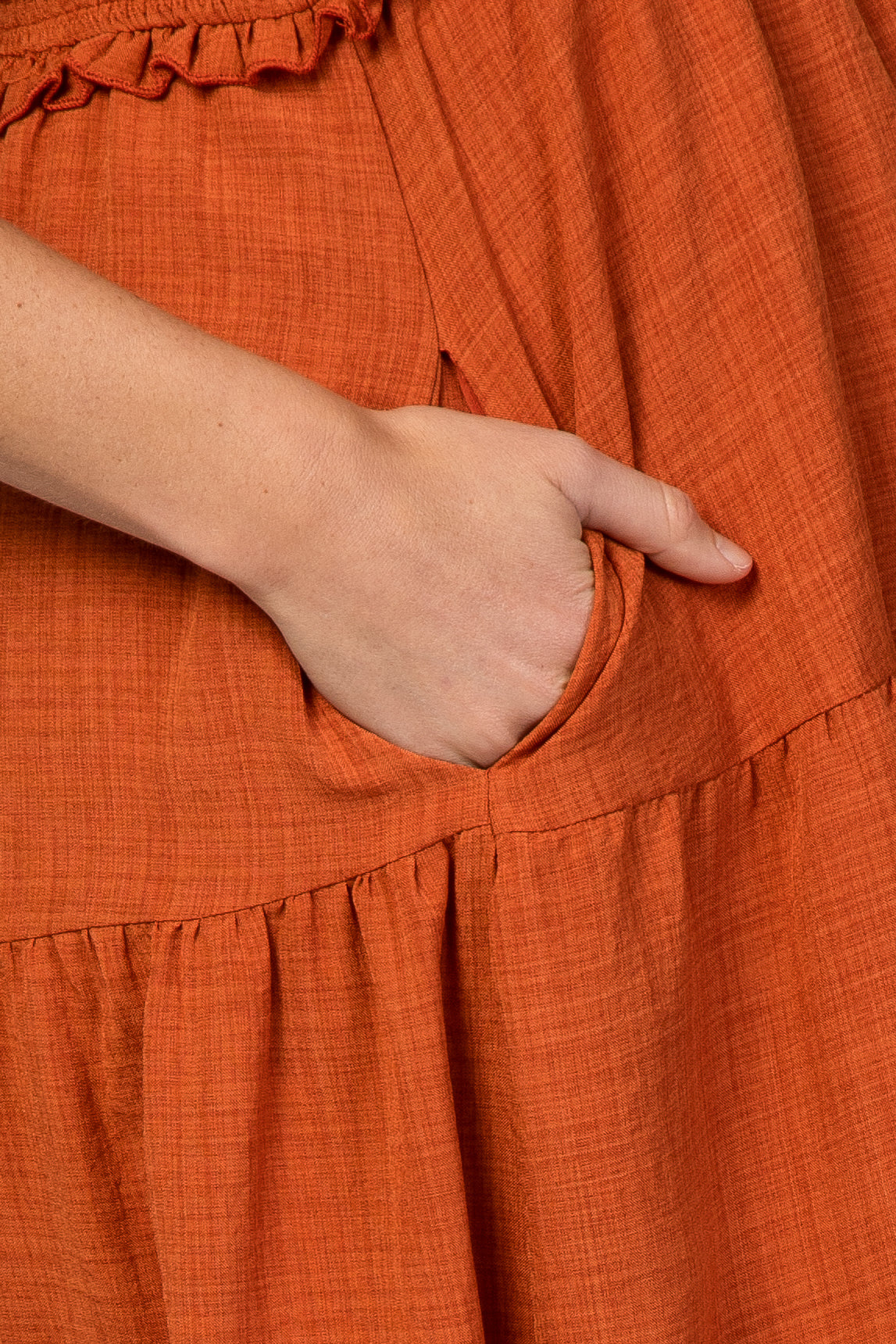 close-up of maternity wear in burnt orange fabric with a ruffle detail and hand in the pocket
