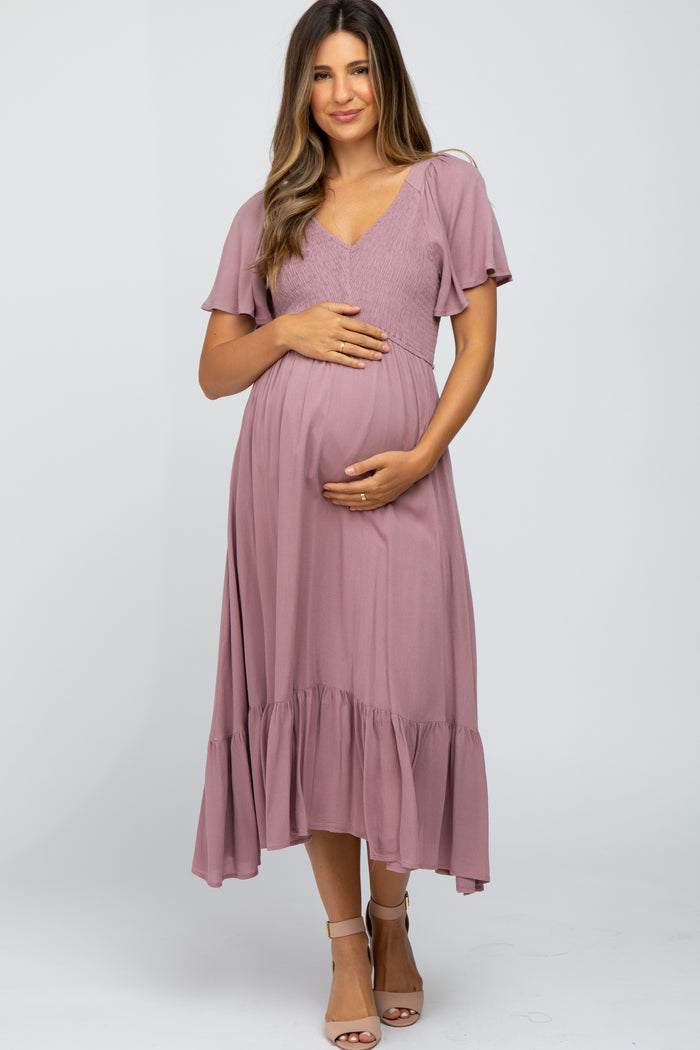 woman wearing a dusty rose maternity dress with short ruffled sleeves and a tiered skirt, holding her baby bump