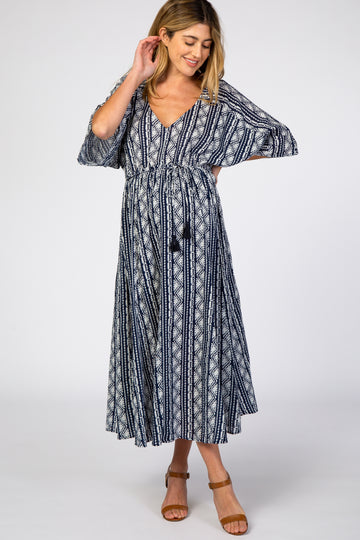 woman wearing a navy blue patterned maternity maxi dress with a v-neckline and tie waist, showcasing her baby bump