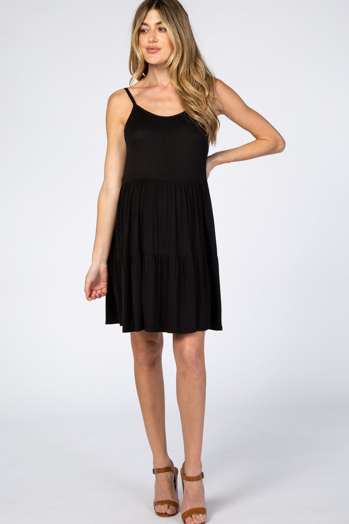 woman wearing a black sleeveless tiered maternity dress and brown strap heels against a white background
