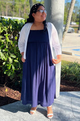woman wearing a navy blue maxi dress with a smocked bodice and white cardigan, standing outdoors