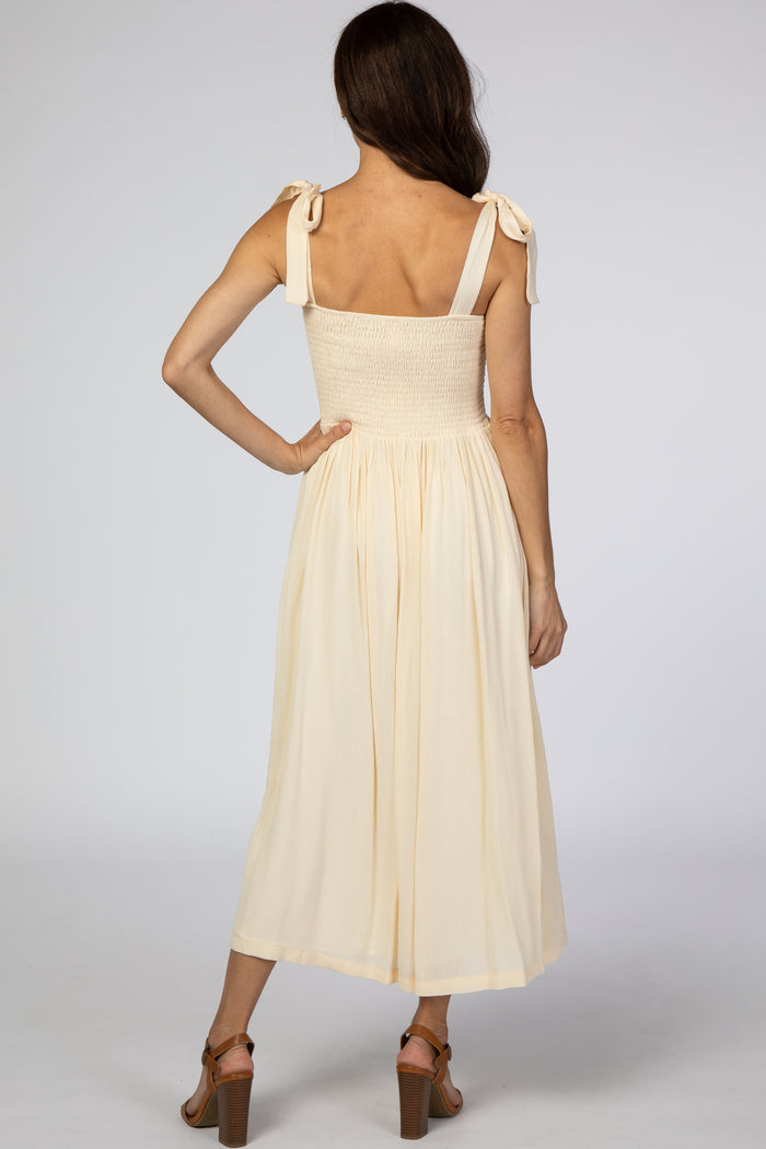 woman wearing a cream smocked back midi dress with tie straps and a flowy skirt