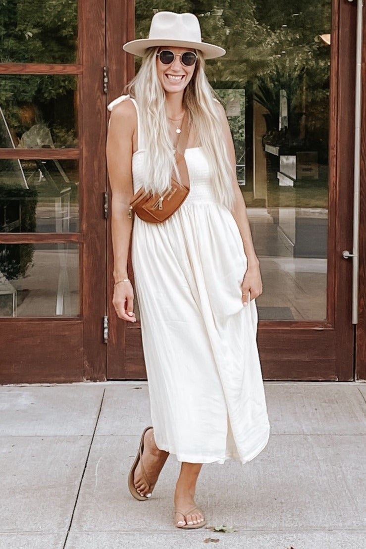 woman wearing a cream sleeveless maxi dress with a front pocket and a brown crossbody bag, smiling outdoors