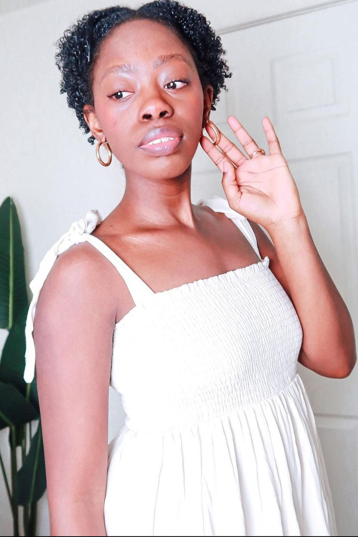 woman wearing a white smocked sundress with adjustable straps and hoop earrings