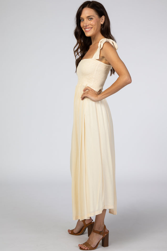woman wearing a light yellow maxi dress with a smocked bodice and tie straps, standing in profile