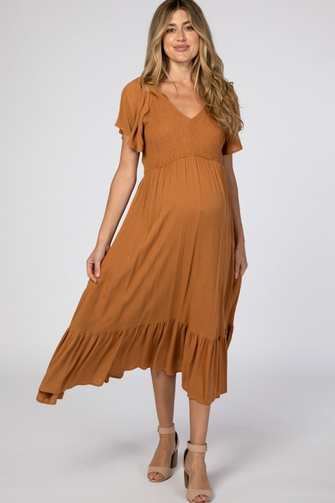 woman wearing a rust-colored maternity dress with a v-neck and ruffled hem, showing her baby bump