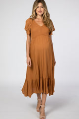 woman wearing a rust-colored maternity dress with flutter sleeves and a ruffled hem, showcasing her baby bump