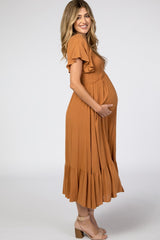 woman wearing an orange maternity dress with ruffled sleeves and a tiered skirt, gently cradling her baby bump