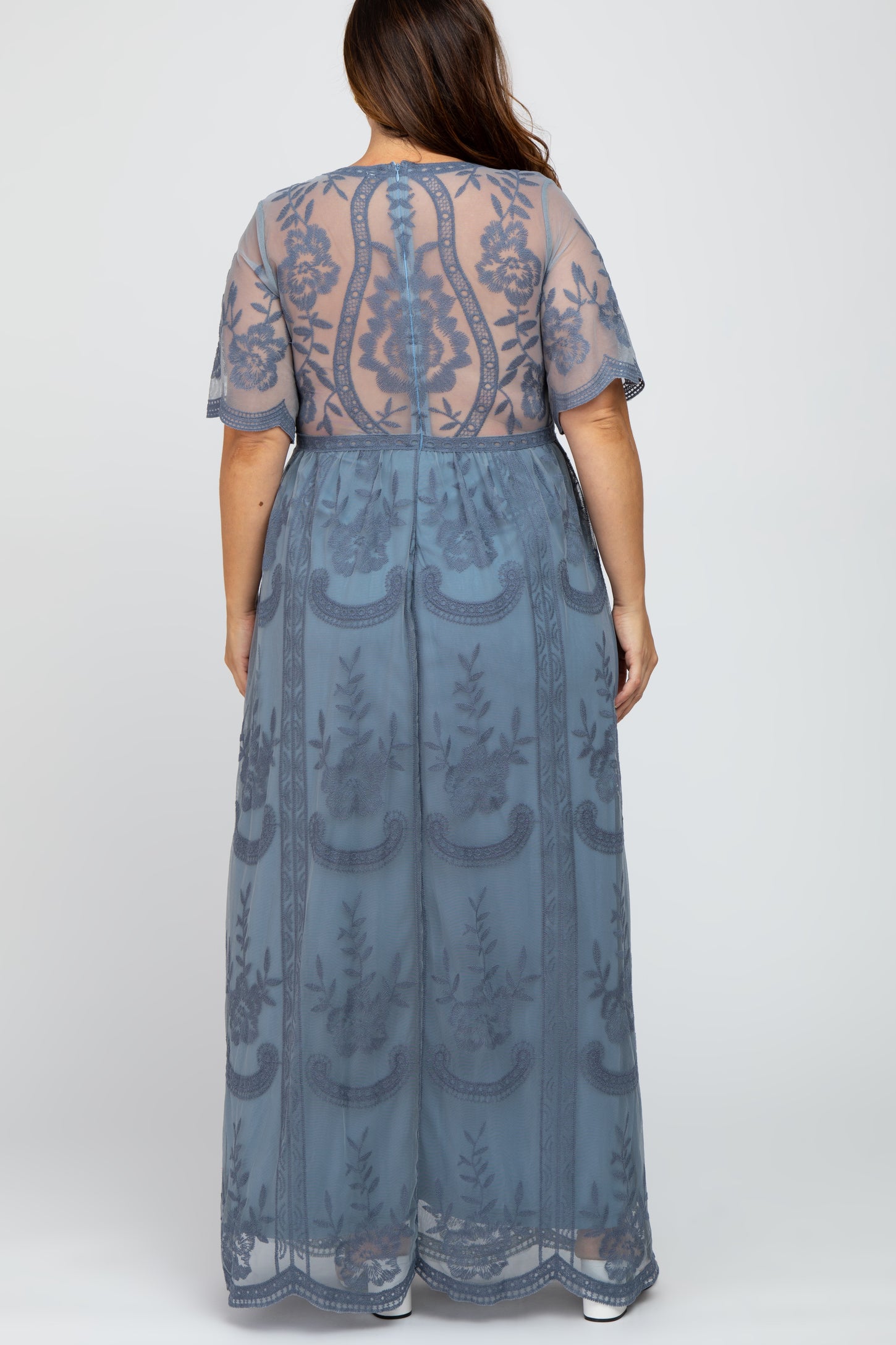 woman wearing a sheer blue plus size maxi dress with floral embroidery and short sleeves, showing the back view