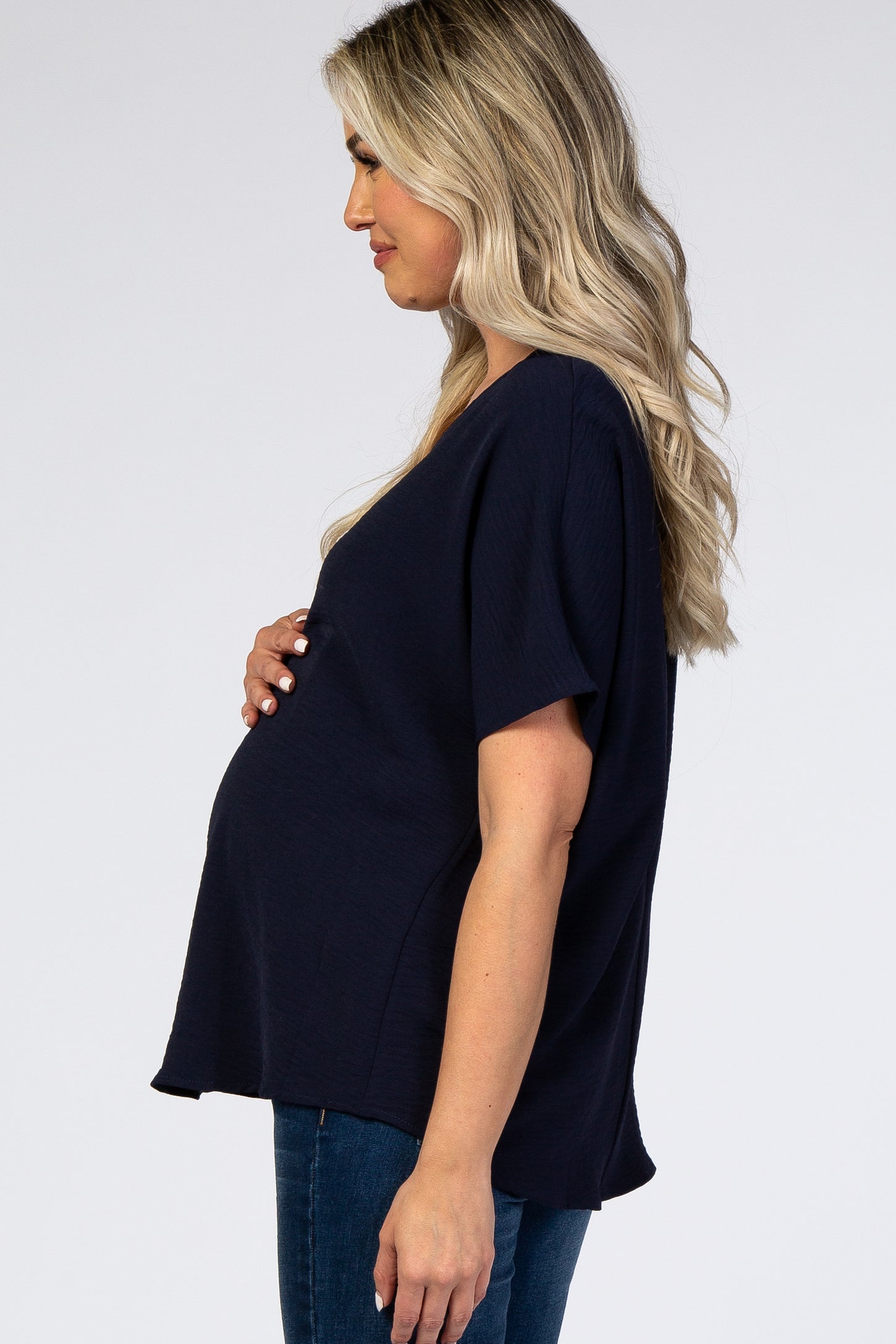 woman wearing a navy blue maternity top, gently holding her baby bump, styled with jeans