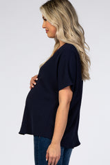woman wearing a navy blue maternity top, gently holding her baby bump, styled with jeans