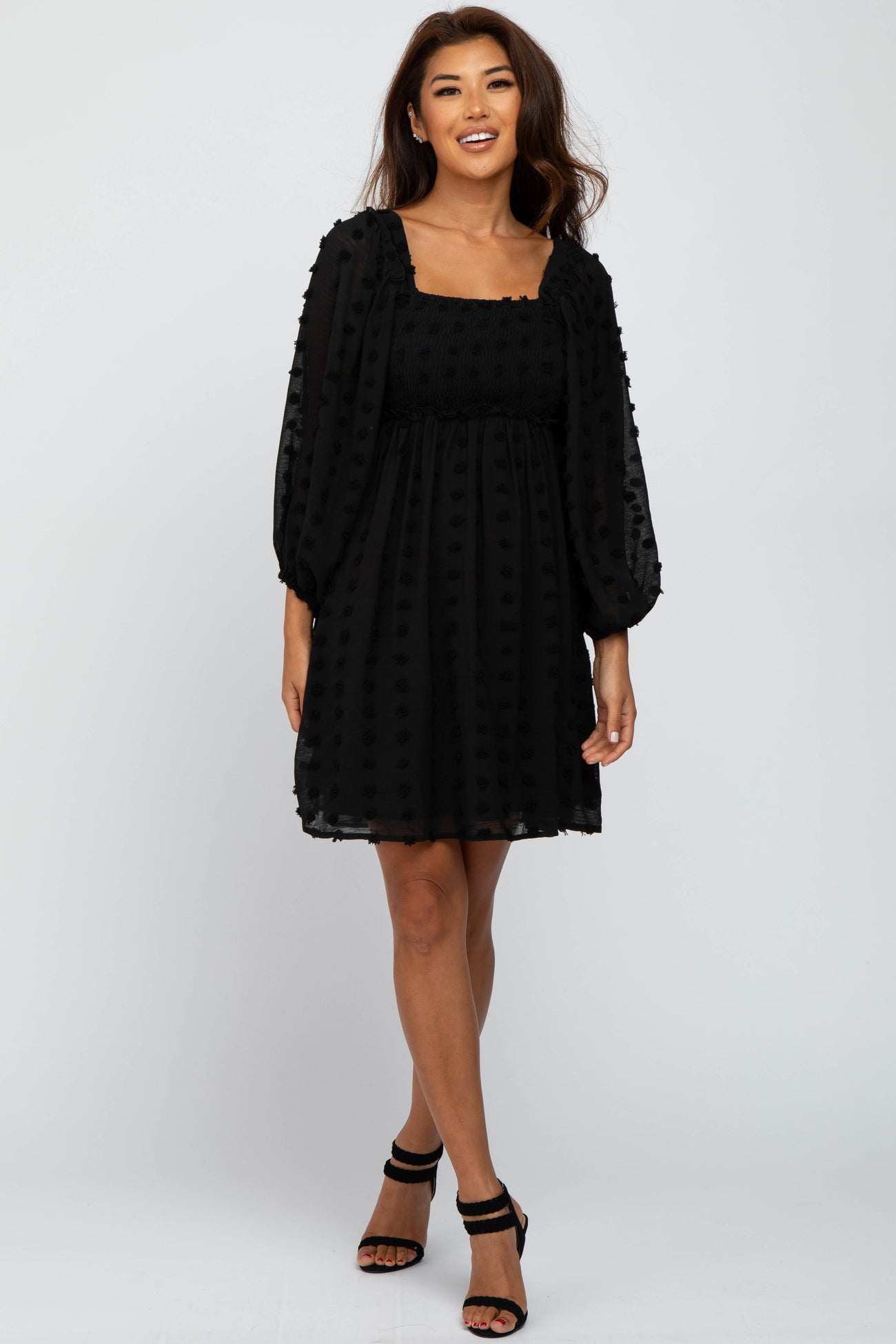 woman wearing a black puff sleeve dress with a textured fabric and flared skirt, standing and smiling