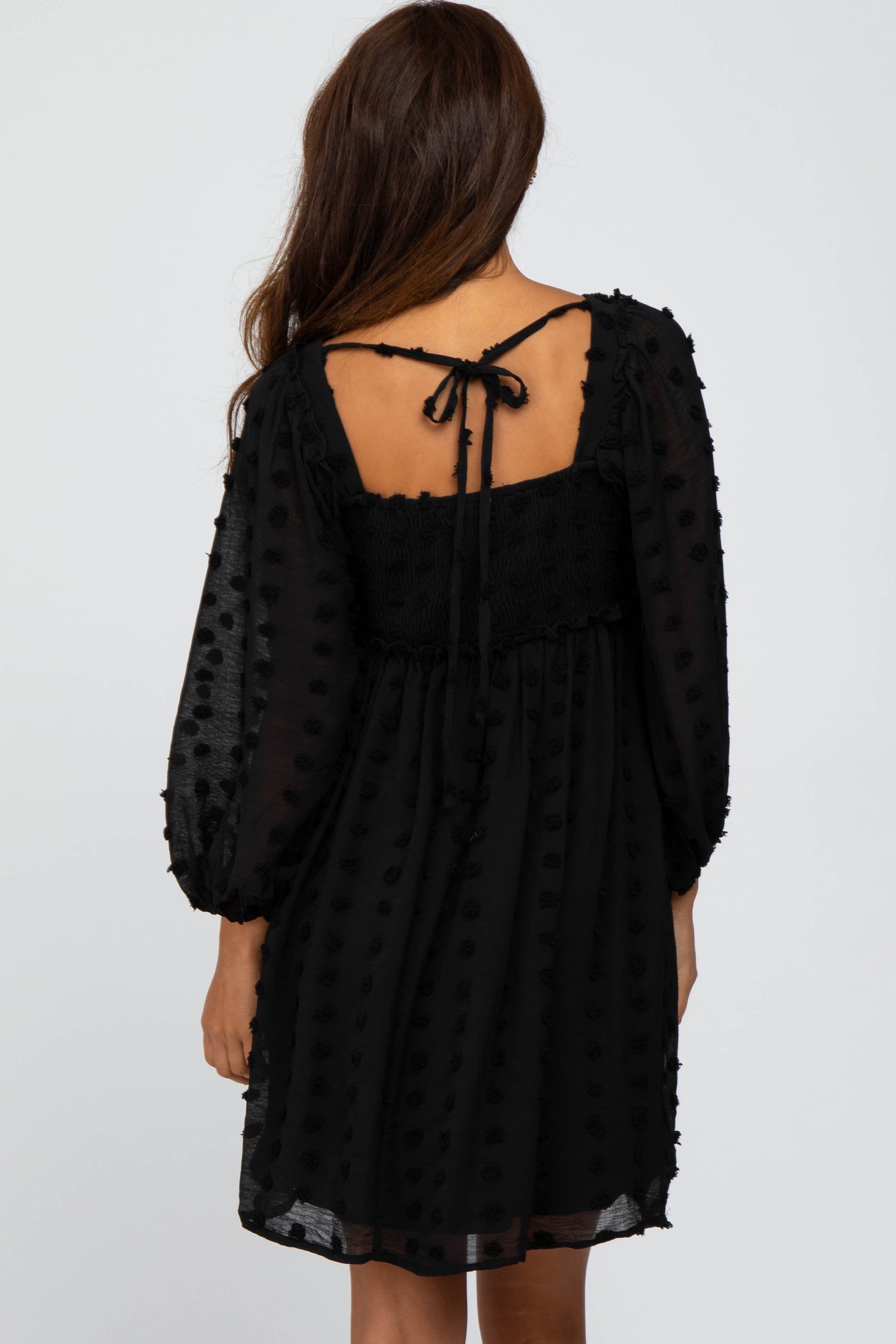woman wearing a black polka dot dress with a smocked bodice and puff sleeves, tie detail at the back