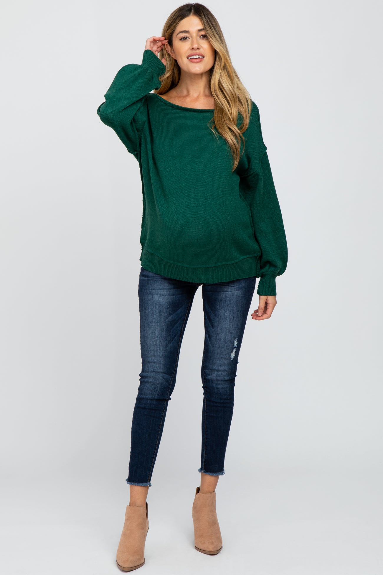 woman wearing a green oversized maternity sweater and blue skinny jeans, showing her baby bump