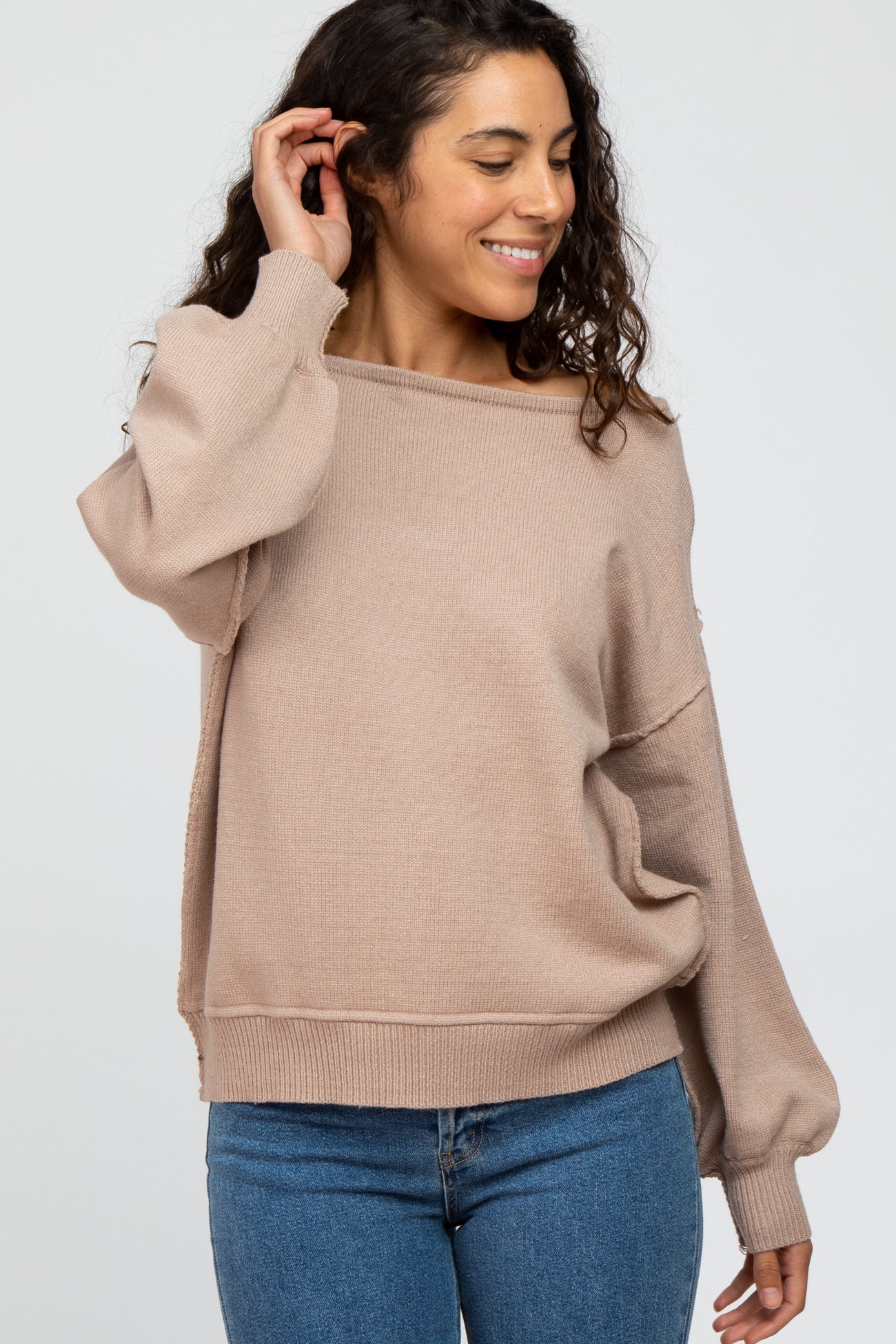 woman wearing a beige oversized sweater with a relaxed fit and wide neckline, paired with blue jeans