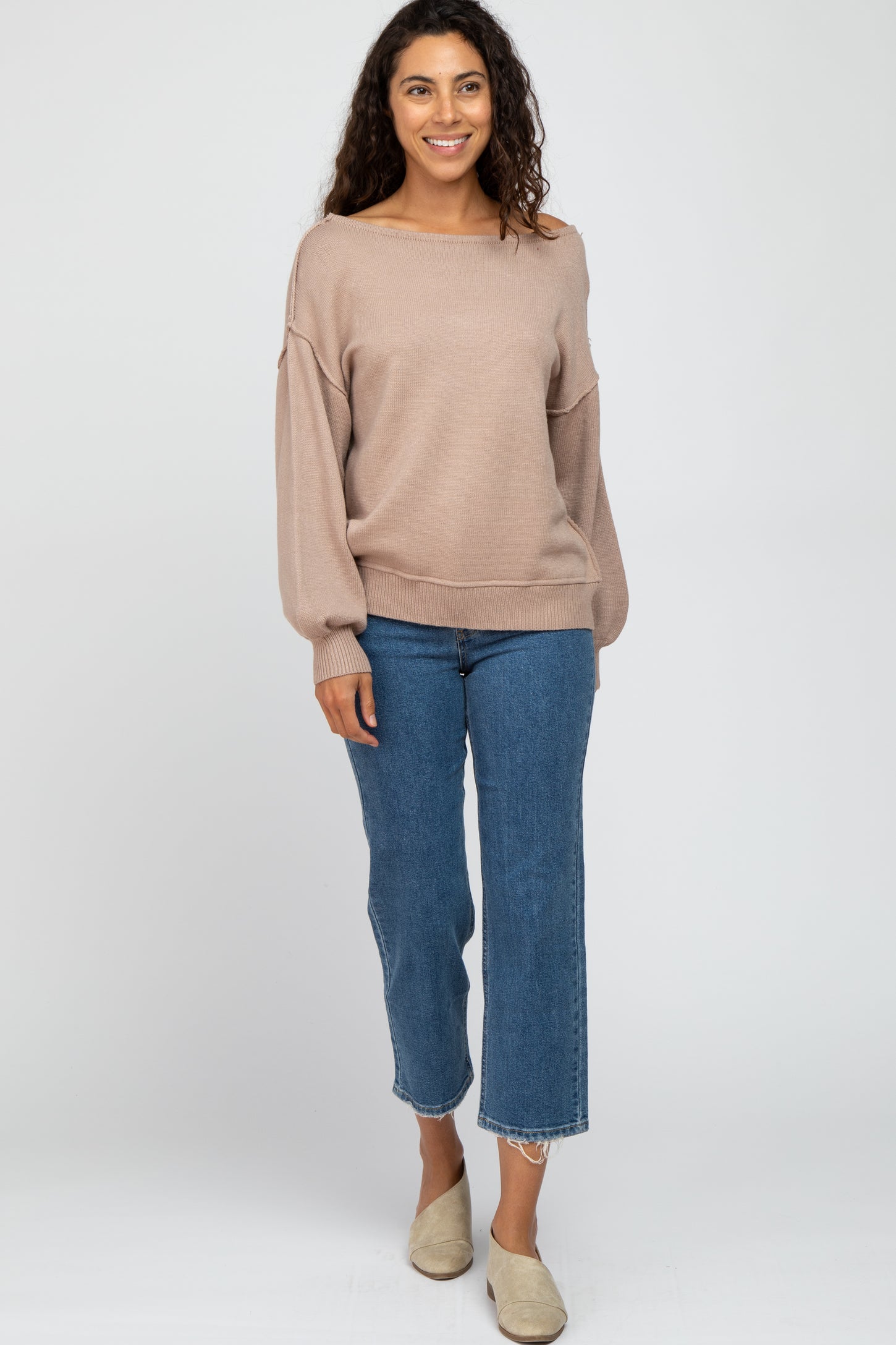 woman wearing a beige oversized sweater and blue cropped jeans with frayed hems