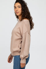 woman wearing a beige long sleeve sweater with a relaxed fit and side seam detailing, paired with blue jeans