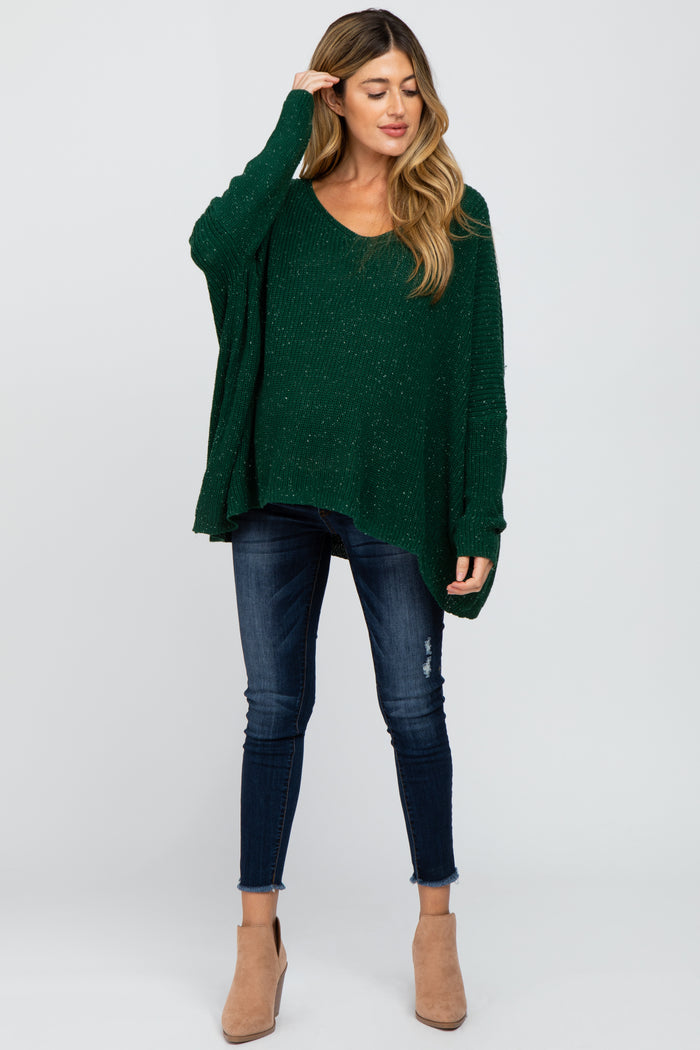 woman wearing a green maternity sweater with a v-neck and relaxed fit paired with dark jeans and ankle boots