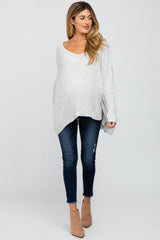woman wearing a light gray oversized maternity sweater and dark blue distressed skinny jeans, showing her baby bump
