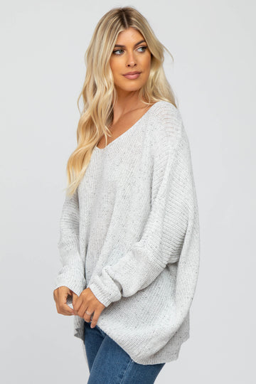 woman wearing a light gray oversized sweater with a v-neck and loose fit, paired with blue jeans