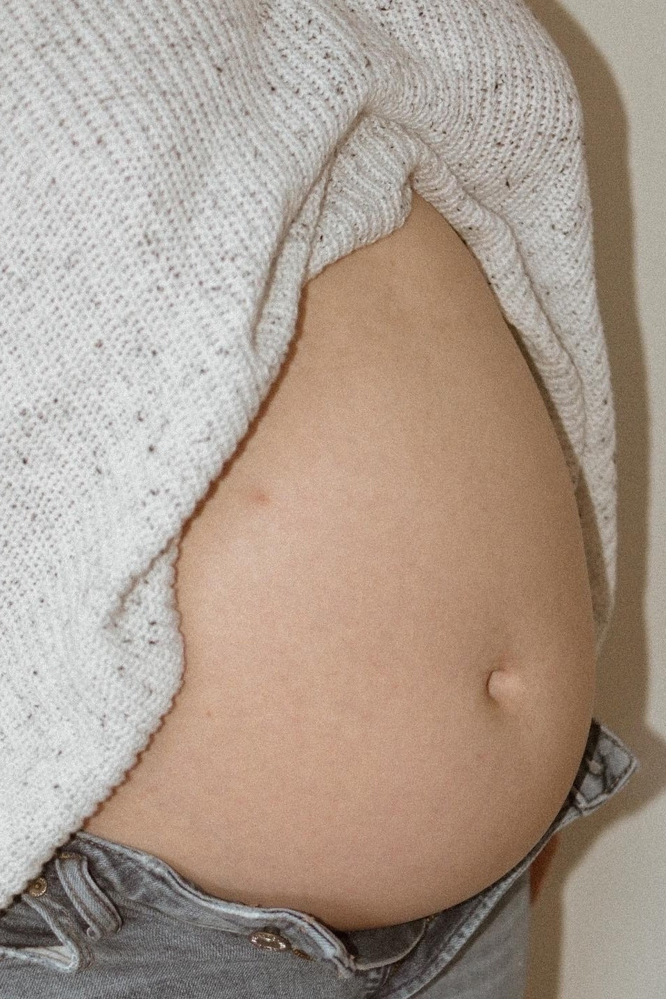 maternity wear showing a visible baby bump in a softly textured white knit sweater paired with gray jeans