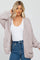 woman wearing a light pink oversized knitted cardigan with pockets over a white top and high-waisted denim jeans