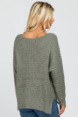 Back view of a woman wearing a sage green textured knit sweater with a scoop neckline and side slits.