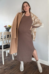 woman wearing a brown ribbed maternity dress with a side slit, styled with a beige coat and scarf, showing her baby bump