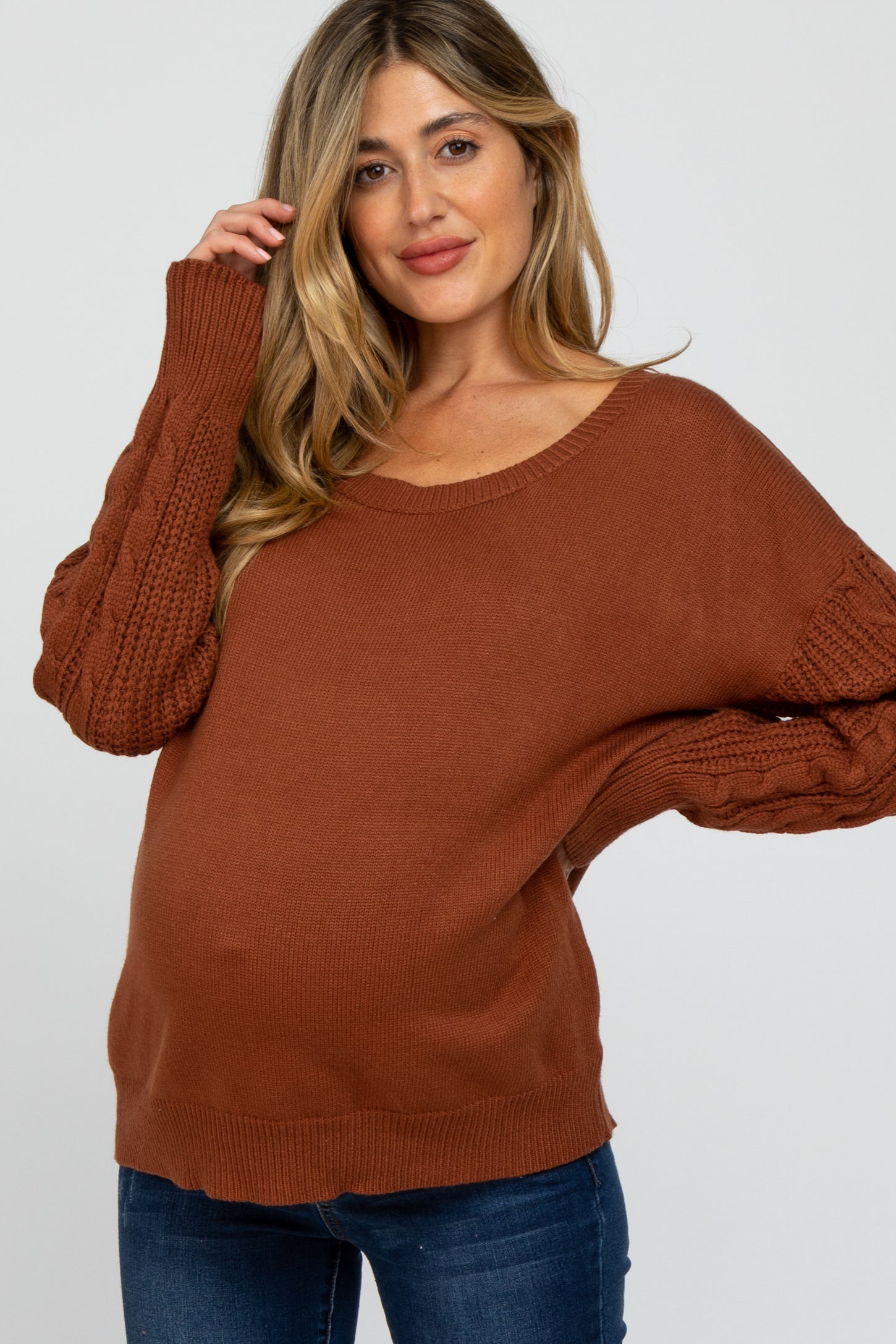 woman wearing a rust-colored maternity sweater with knitted sleeves and a visible baby bump
