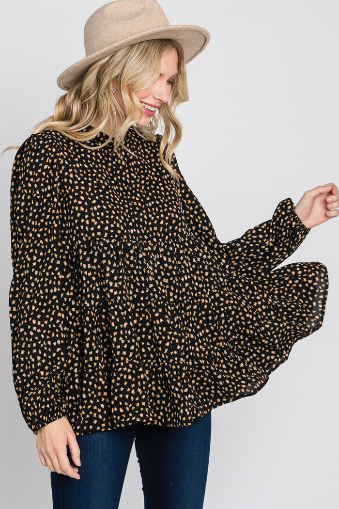 woman wearing a black and tan polka dot button-up shirt with a flowy silhouette and long sleeves, smiling while wearing a hat