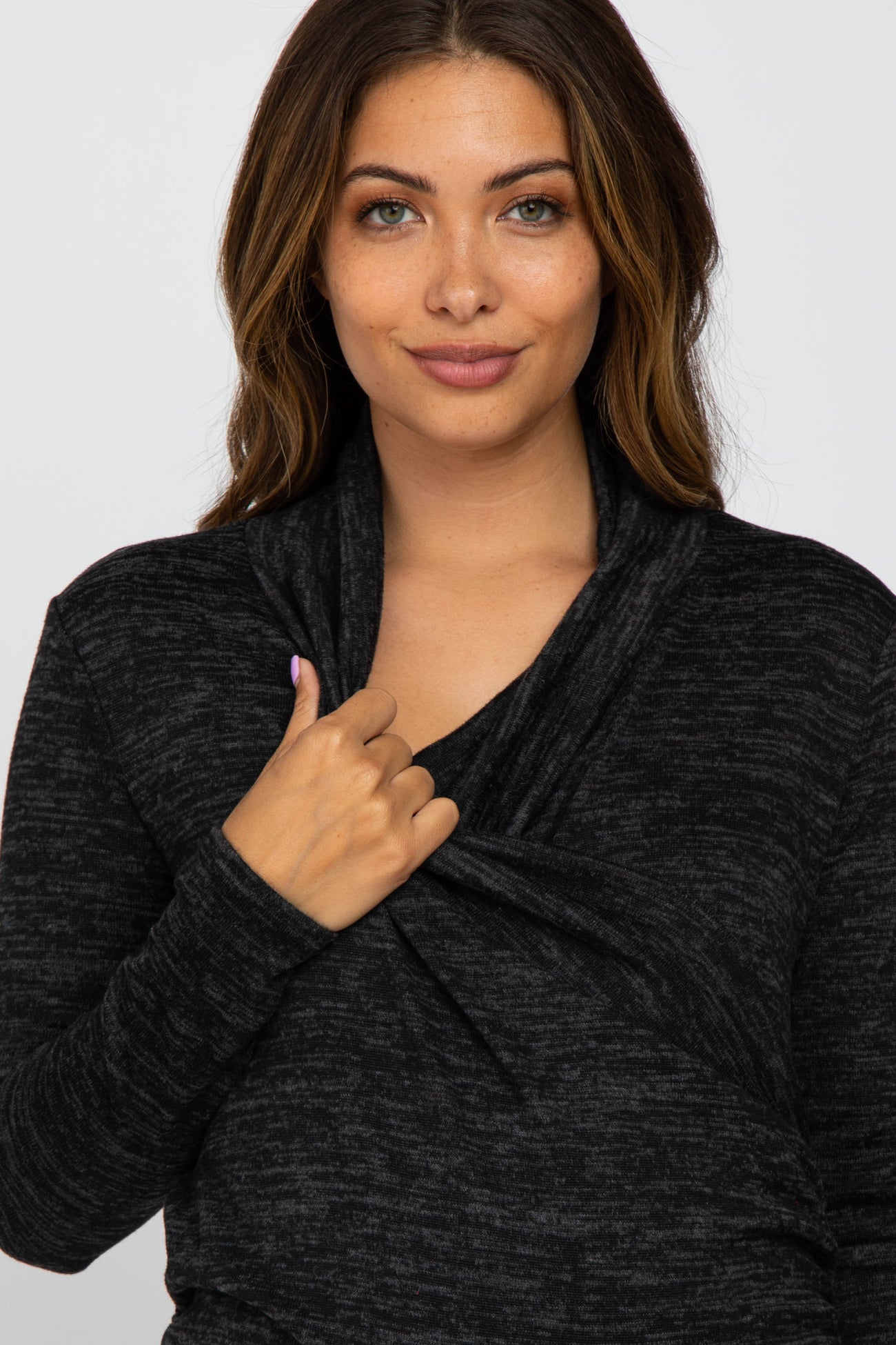 woman wearing a black maternity wrap top with long sleeves and a draped neckline, highlighting her baby bump