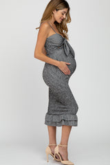 woman wearing a gray and white striped maternity dress with a bow detail and ruffled hem, holding her baby bump