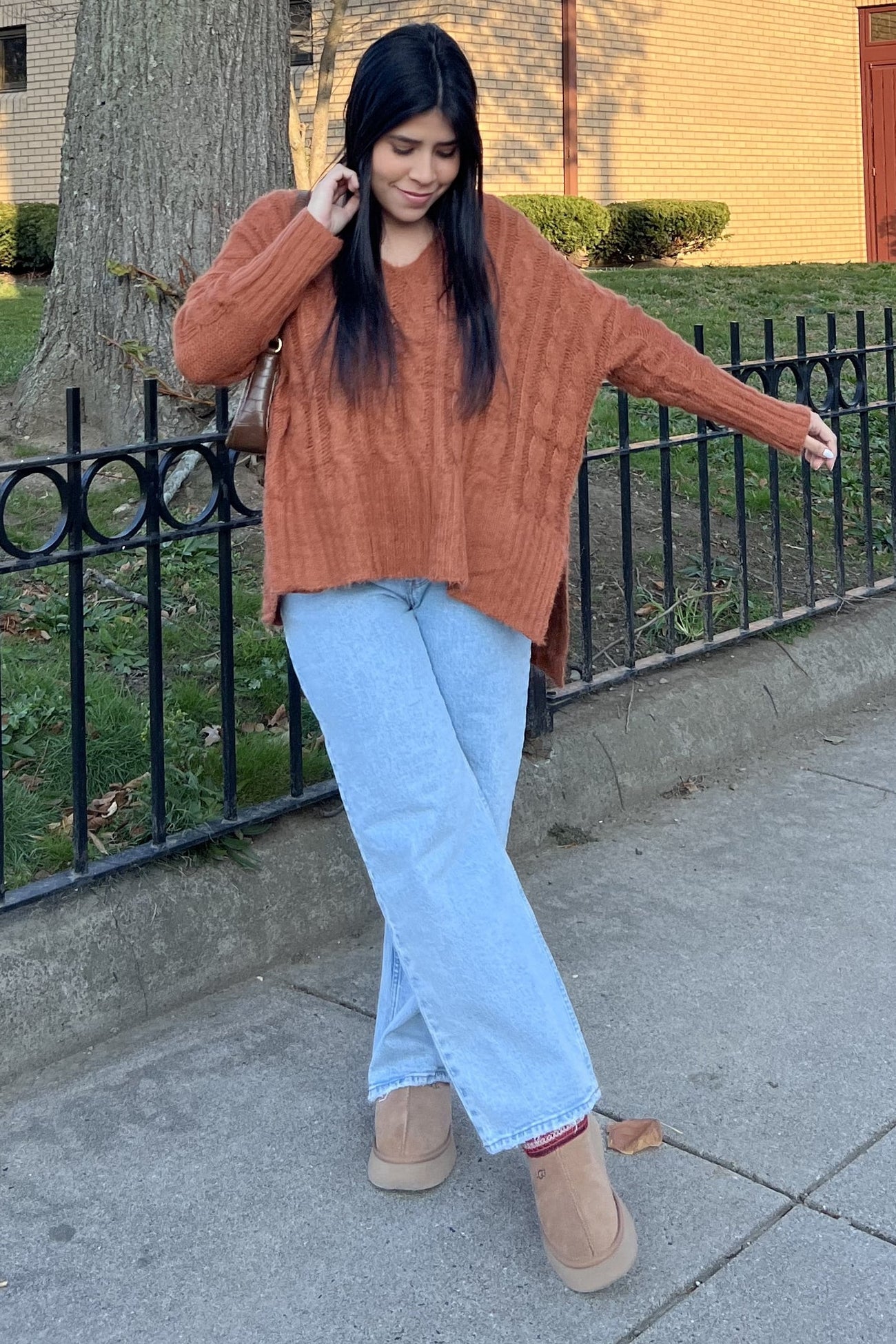 woman wearing a rust orange oversized cable knit sweater and light blue wide-leg jeans with tan ankle boots