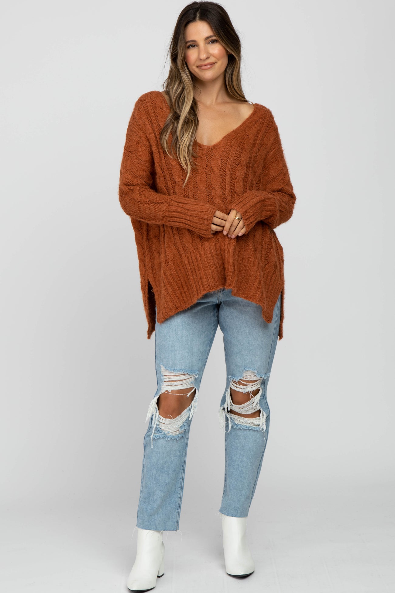 woman wearing an oversized rust-colored cable knit maternity sweater with v-neck and paired with distressed light blue jeans