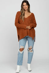 woman wearing an oversized rust-colored cable knit maternity sweater with v-neck and paired with distressed light blue jeans